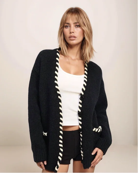 Woman wearing a black cardigan with white trim on a plain background