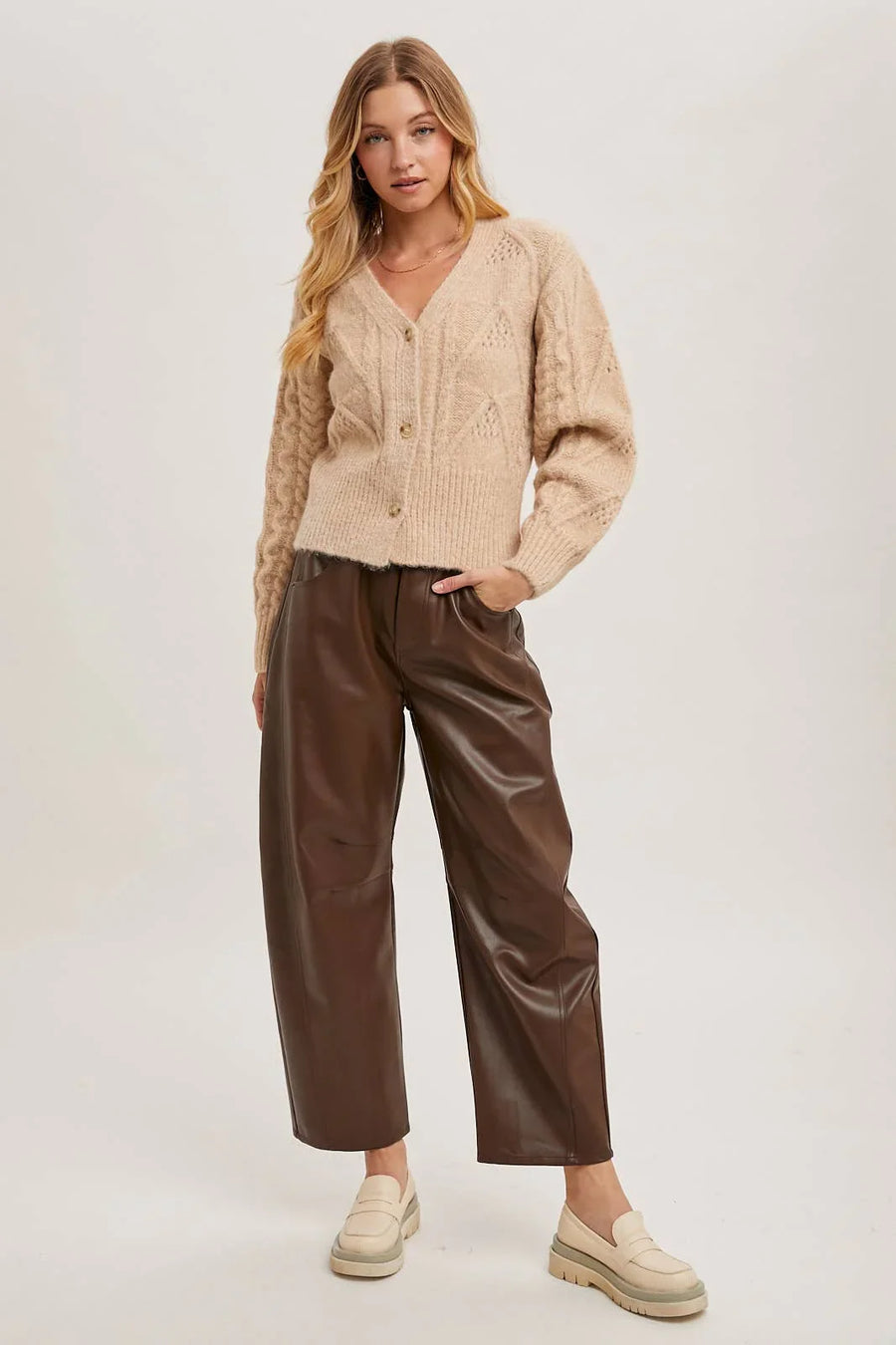 Woman wearing a beige cardigan and brown pants on a white background