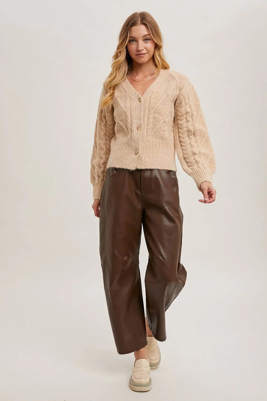 Woman wearing a beige cardigan and brown pants on a white background