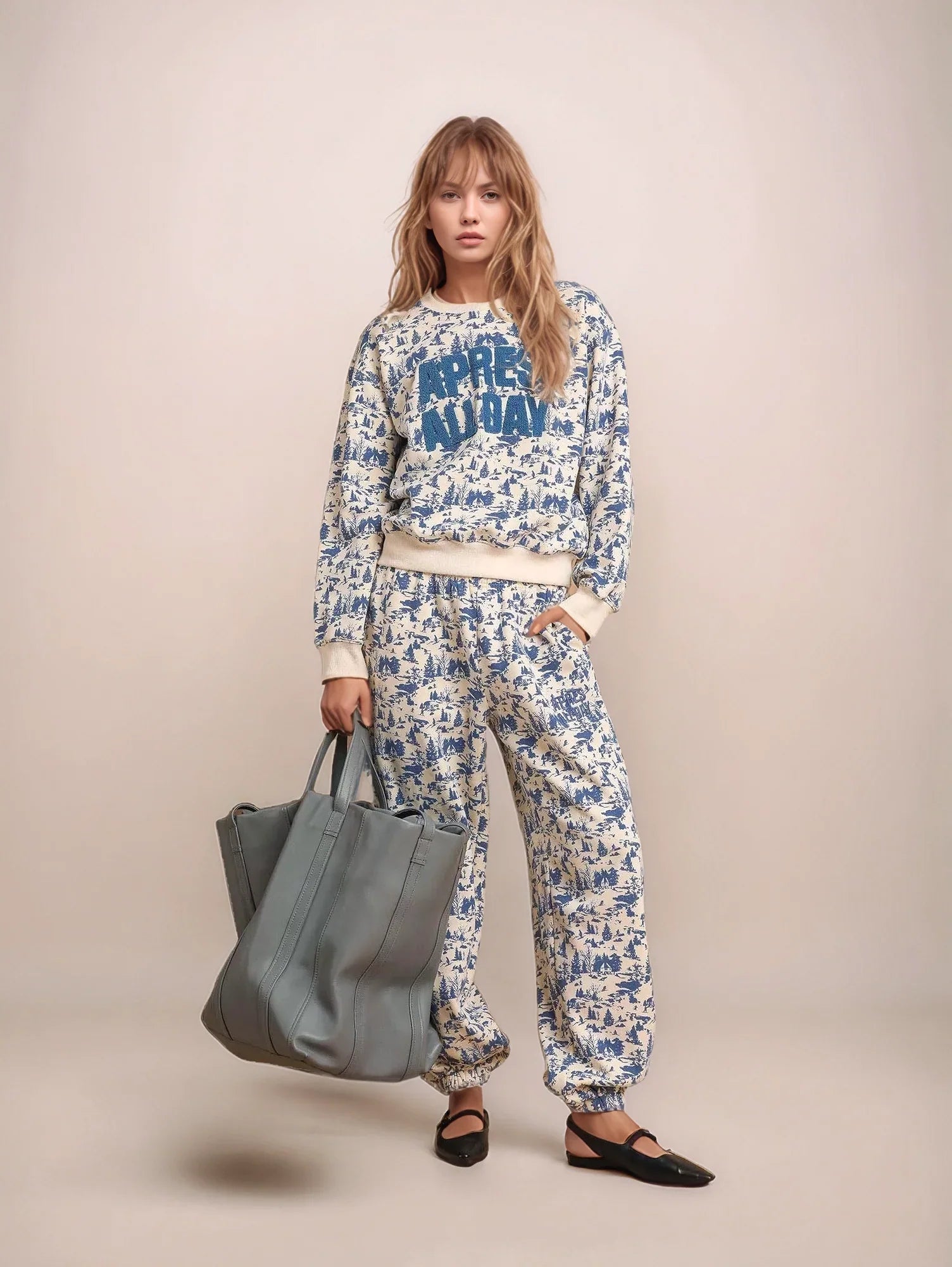 Woman wearing a floral outfit with a text sweater, holding a gray bag on a beige background