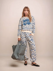 Woman wearing a floral outfit with a text sweater, holding a gray bag on a beige background