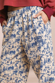 Beige pants with blue forest pattern worn by a person, on a beige background