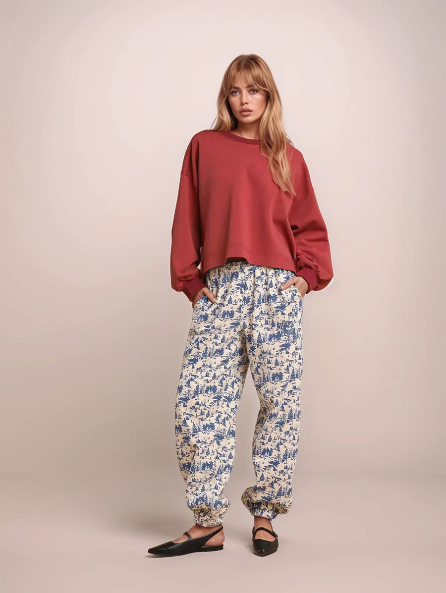 Woman wearing a red sweater and floral pants on a plain background