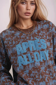 Person wearing a sweater with 'APRES ALL DAY' text in blue on a patterned background