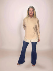 a blonde woman wearing a beige layered look turtleneck sweater with pinstriped shirt hem and dark blue jeans
