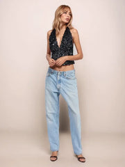 Woman wearing a black sequin top and light blue jeans against a beige background