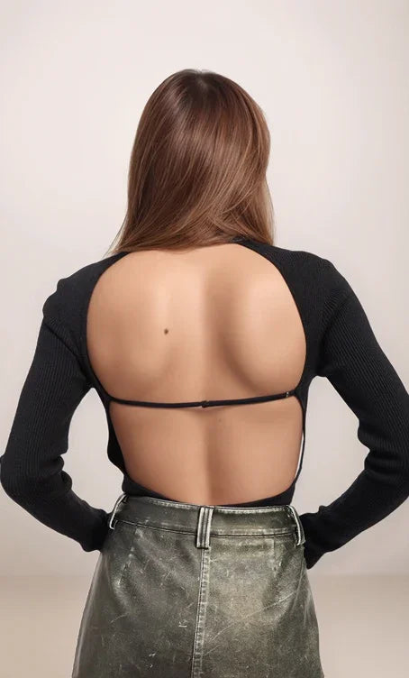 Person wearing a black long-sleeve top with open back and gray pants on a plain background