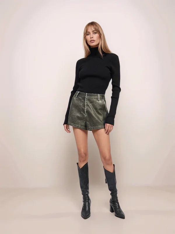 Woman wearing a black turtleneck, green leather skirt, and black knee-high boots on a plain background