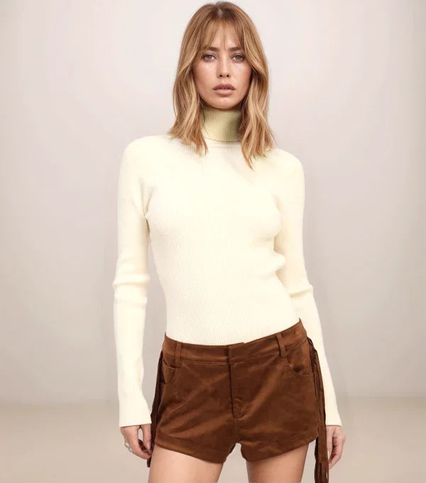 Woman wearing a white turtleneck and brown shorts against a plain background