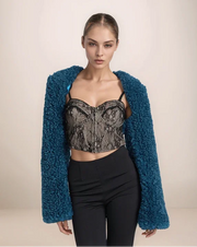 Model wearing a blue textured cardigan, black lace top, and black pants on a beige background