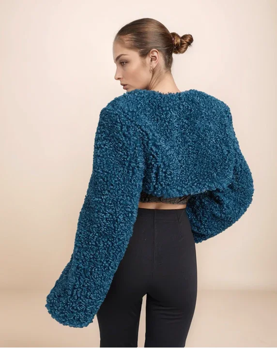 Woman wearing a blue textured cardigan and black pants on a beige background