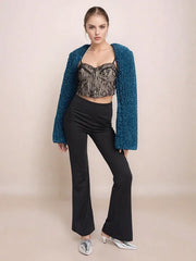 Woman wearing a teal cardigan, black top, and pants on a beige background