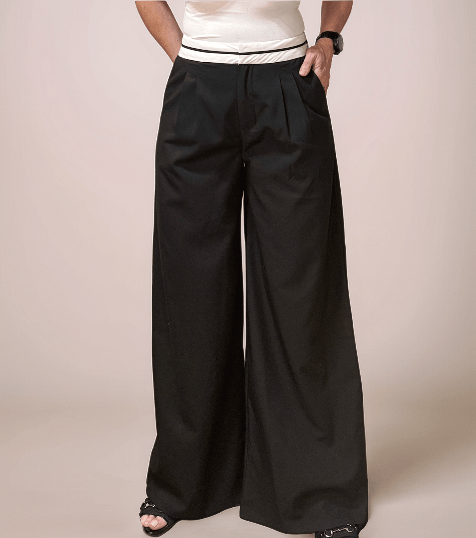 a woman is wearing black relaxed fit trousers that have a white contrast waistband. she has one hand in a pocket. the trousers could be dressed up or down for multiple looks.