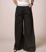 a woman is wearing black relaxed fit trousers that have a white contrast waistband. she has one hand in a pocket. the trousers could be dressed up or down for multiple looks.
