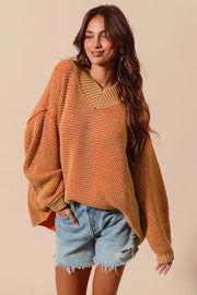 Woman wearing a orange and tan knitted sweater and denim shorts against a beige background