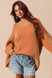 Woman wearing an orange sweater and denim shorts against a beige background