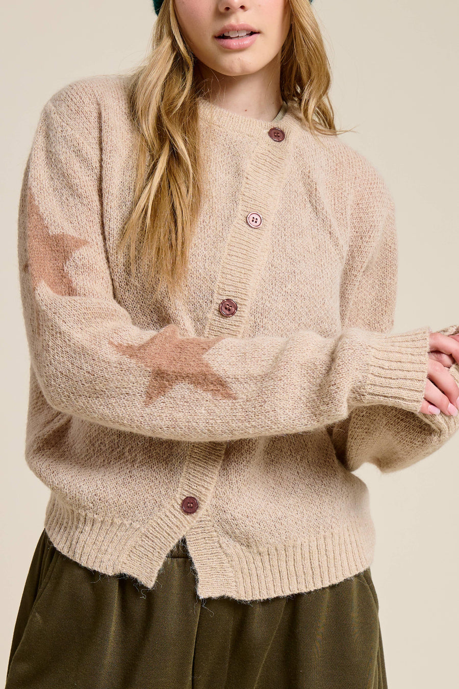 Person wearing a beige cardigan with star patterns on a plain background