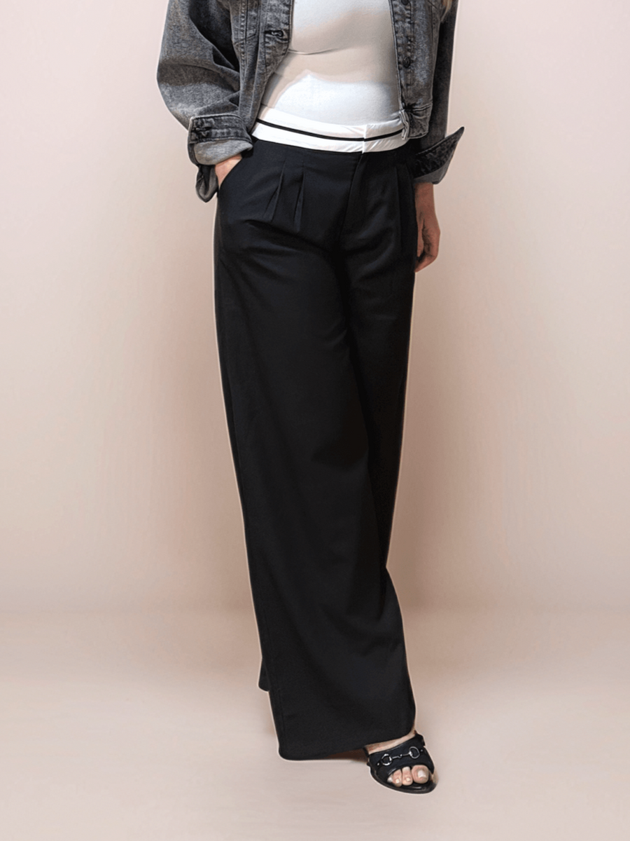 a blonde woman is wearing black relaxed fit trousers that feature a white contrasting waistband. She is also wearing a white tank top and a gray jean jacket.