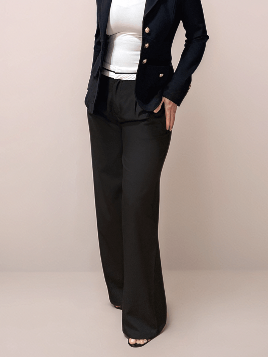 A blonde woman wearing glasses is wearing black relaxed fit trousers that have a white contrasting waistband. She is also wearing a white top and a black blazer