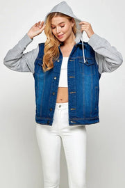 Woman wearing a dark blue denim vest over a gray hoodie with white jeans and white crop top and has the hood pulled up