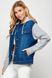 Woman wearing a dark wash denim vest over a gray hoodie on a white background