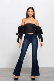 Woman wearing a black off-shoulder top and blue flared jeans on a white background