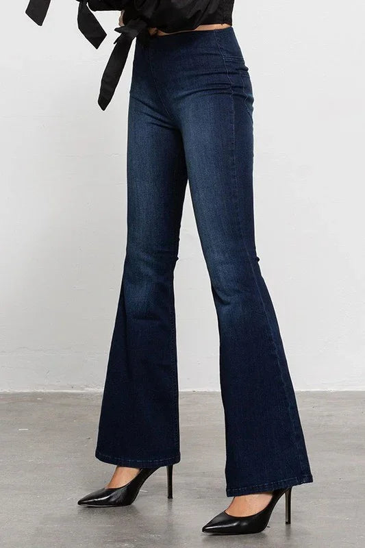 Dark blue flared jeans worn with black high-heeled shoes on a plain background