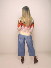 Person wearing a colorful patterned sweater and blue jeans on a plain background