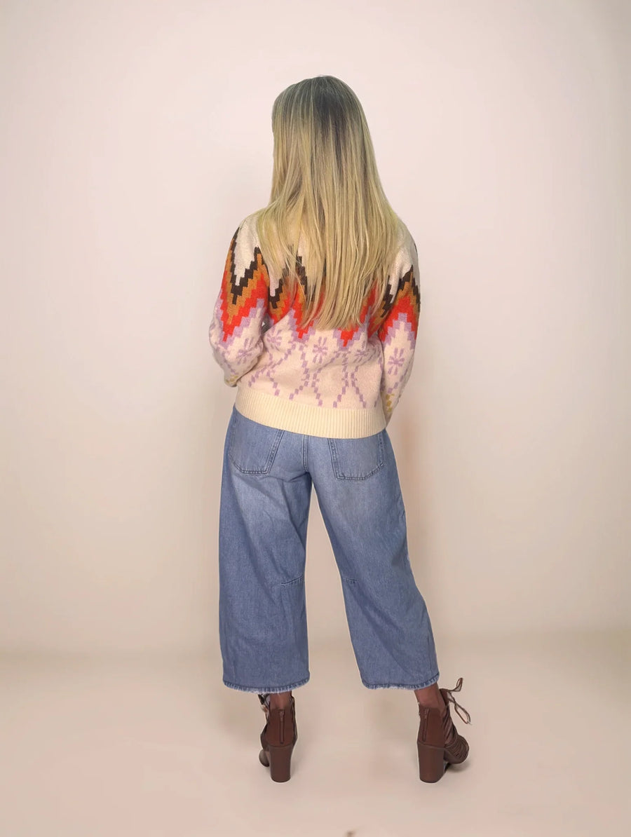 Person wearing a colorful patterned sweater and blue jeans on a plain background