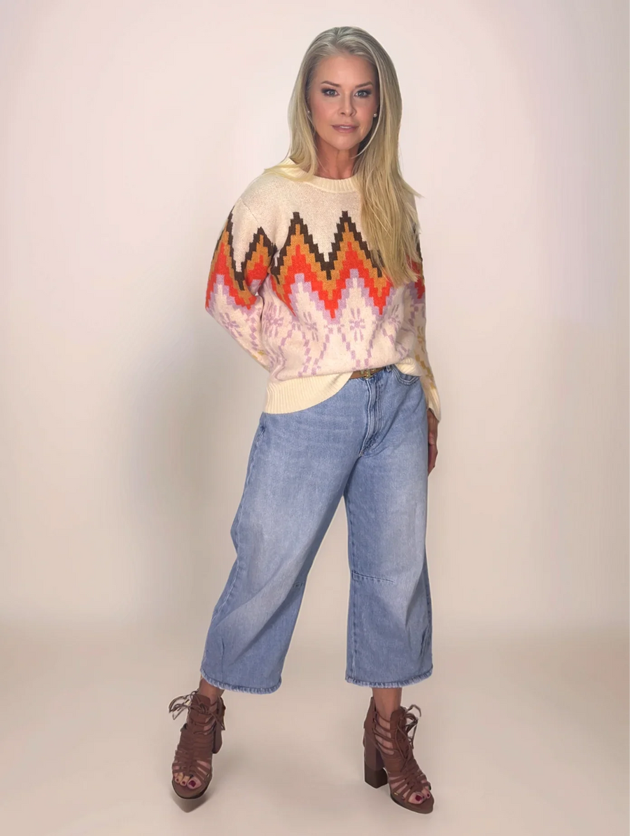 Person wearing a colorful sweater with geometric pattern and blue jeans on a plain background