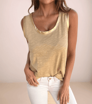 a woman with dark hair is wearing a tan tan top that has metallic trim at the armholes and neckline with white jeans