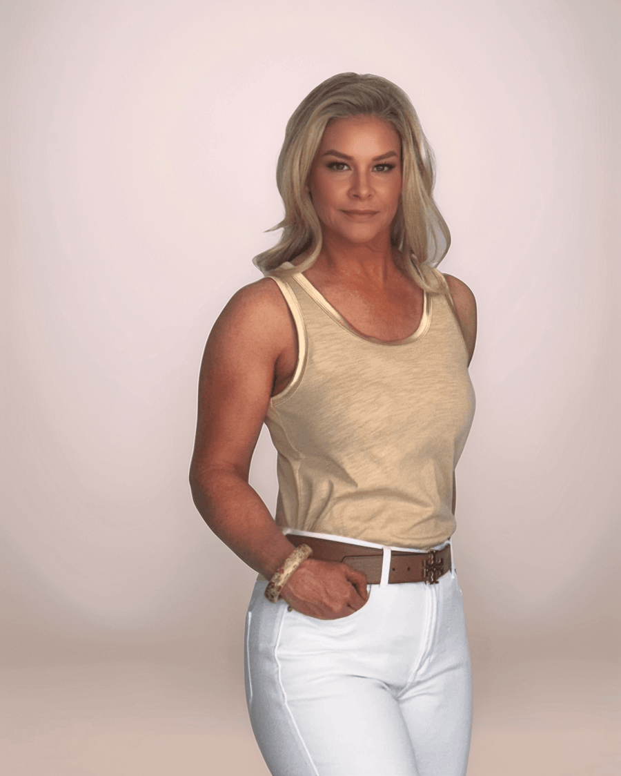a blonde woman is wearing a tan colored tank top with metallic gold trim at the armholes and neckline. she has it pared with white jeans and a brown belt.