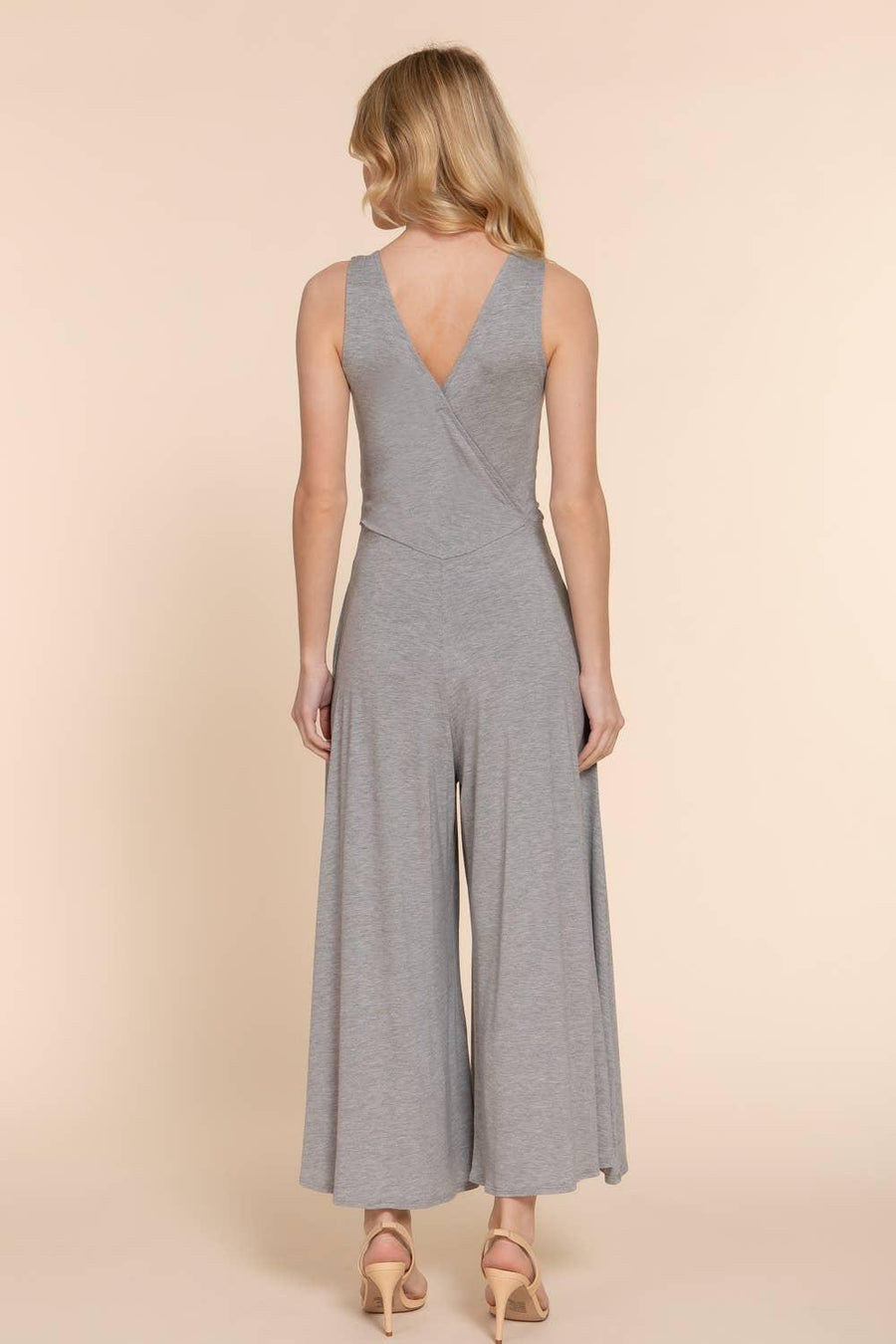 a blonde woman modeling the back of a gray sleeveless knit surplice jumpsuit