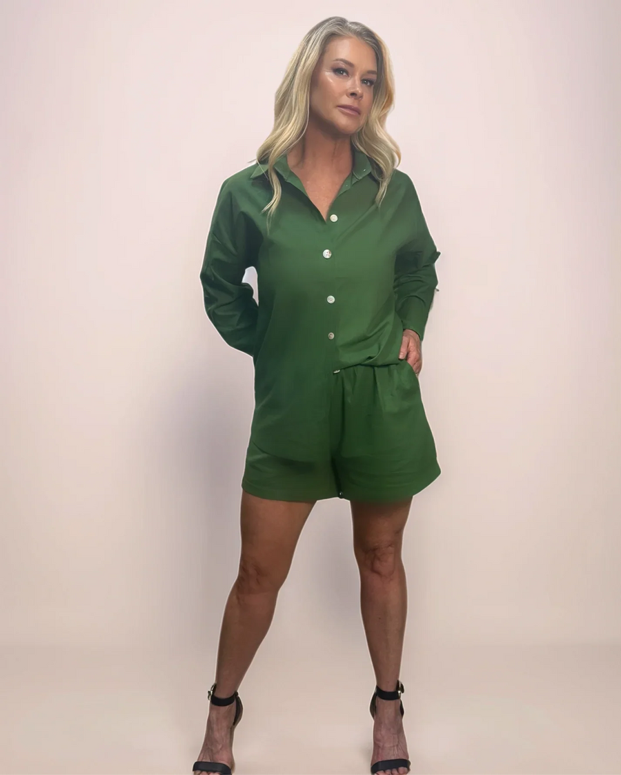 a stylish blonde woman is wearing a comfortable and classy green button down shirt and short set with black sandals.