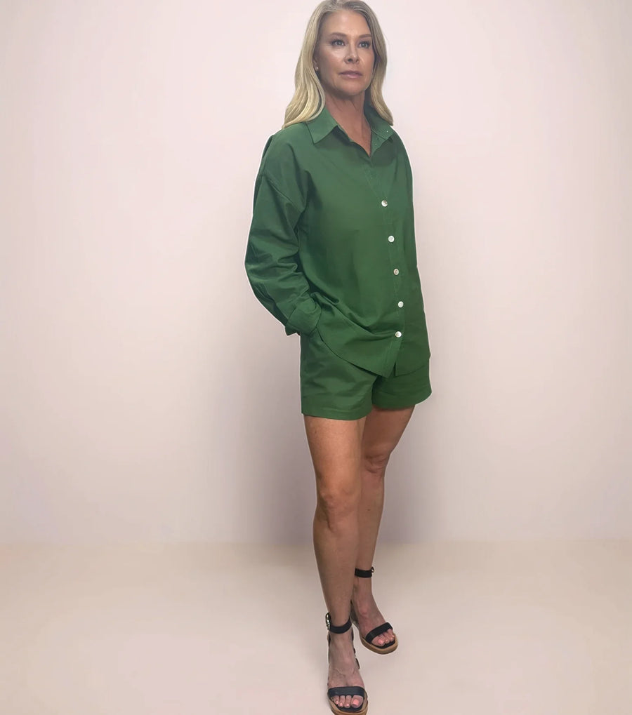 a stylish blonde woman is wearing a matching green button down shirt and shorts set with black sandals