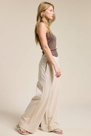 Woman wearing a brown top and beige wide-leg pants on a plain background