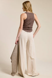 Woman wearing a brown sleeveless top and beige wide-leg pants on a plain background