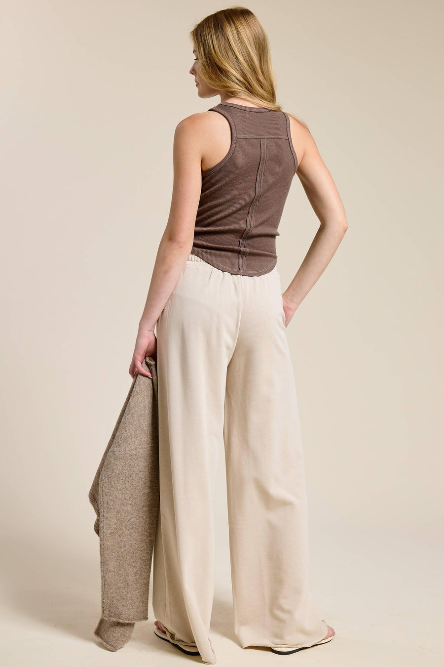 Woman wearing a brown sleeveless top and beige wide-leg pants on a plain background