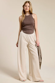 Woman wearing a brown sleeveless top and beige wide-leg pants against a plain background