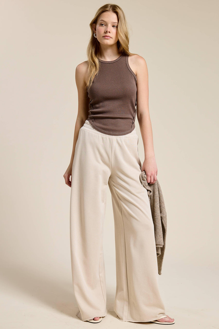 Woman wearing a brown sleeveless top and beige wide-leg pants against a plain background