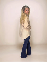 a blonde woman looking back towards the camera in a layered look beige sweater with a pinstripe long hem in the back and shorter hem in the front.