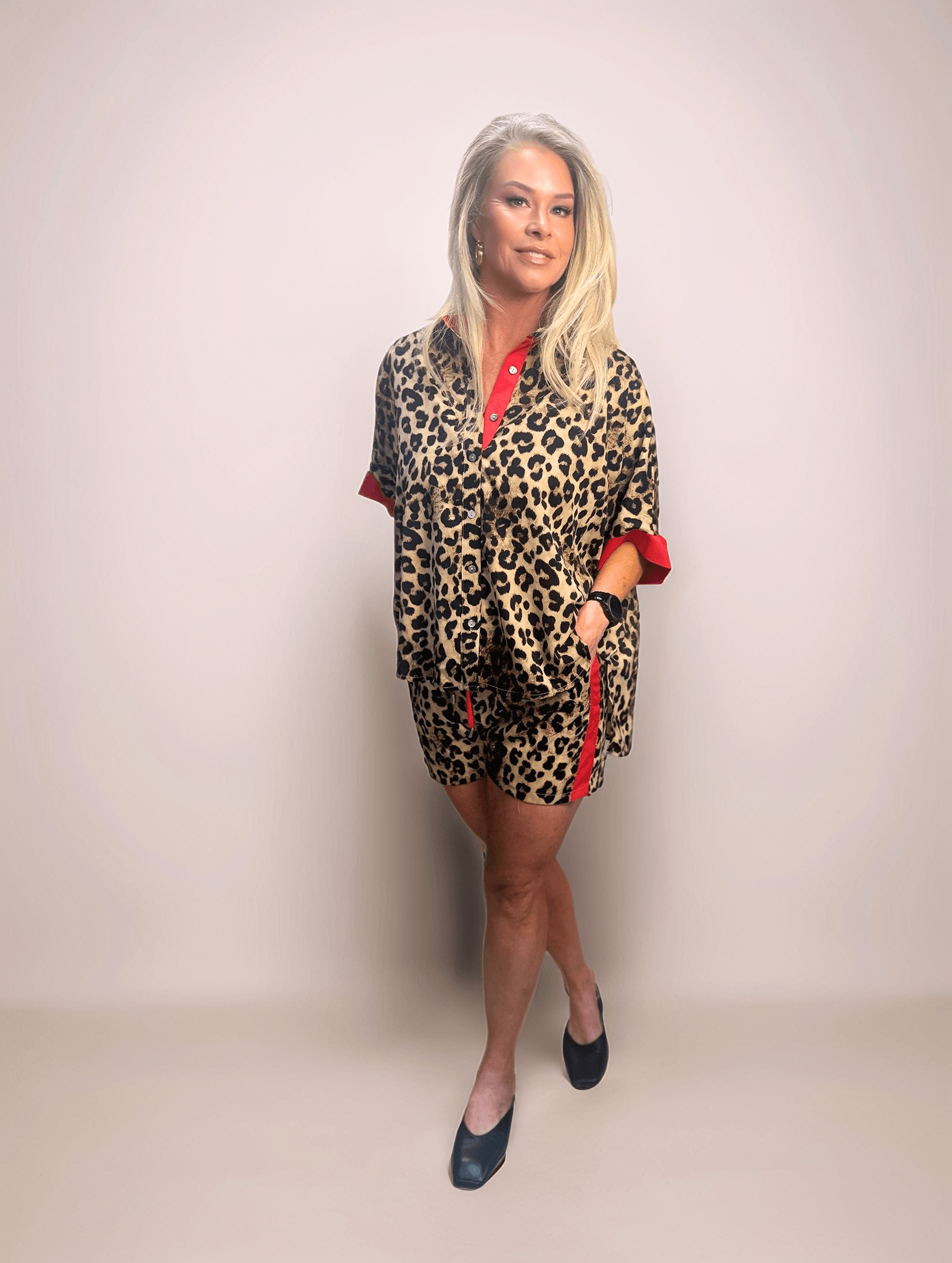 Fashionable blonde woman modeling a comfortable and chic leopard print shorts and button down shirt set featuring red contrasting details, perfect for a casual yet trendy look.