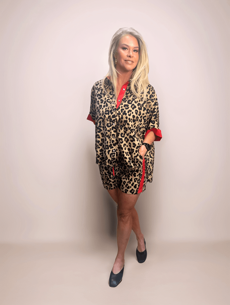 Fashionable blonde woman modeling a comfortable and chic leopard print shorts and button down shirt set featuring red contrasting details, perfect for a casual yet trendy look.