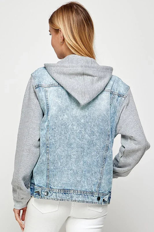 Person wearing a light wash denim jacket with a gray hoodie on a white background