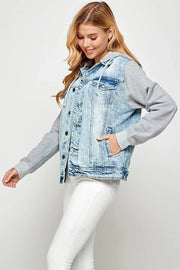 Woman wearing a light blue denim jacket over a gray hoodie over white jeans with one hand in her pocket.