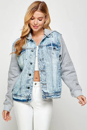 Woman wearing a light blue acid wash denim jacket over a gray hoodie with white jeans and a crop top