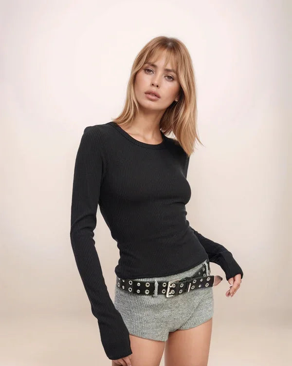 Woman wearing a black long-sleeve top and checkered shorts with a belt on a beige background