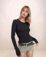 Woman wearing a black long-sleeve top and checkered shorts with a belt on a beige background