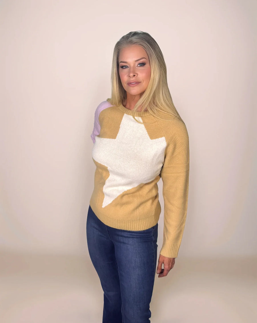blonde woman is wearing a colorblock sweater in camel and pink with a cream star on the front and dark wash jeans.