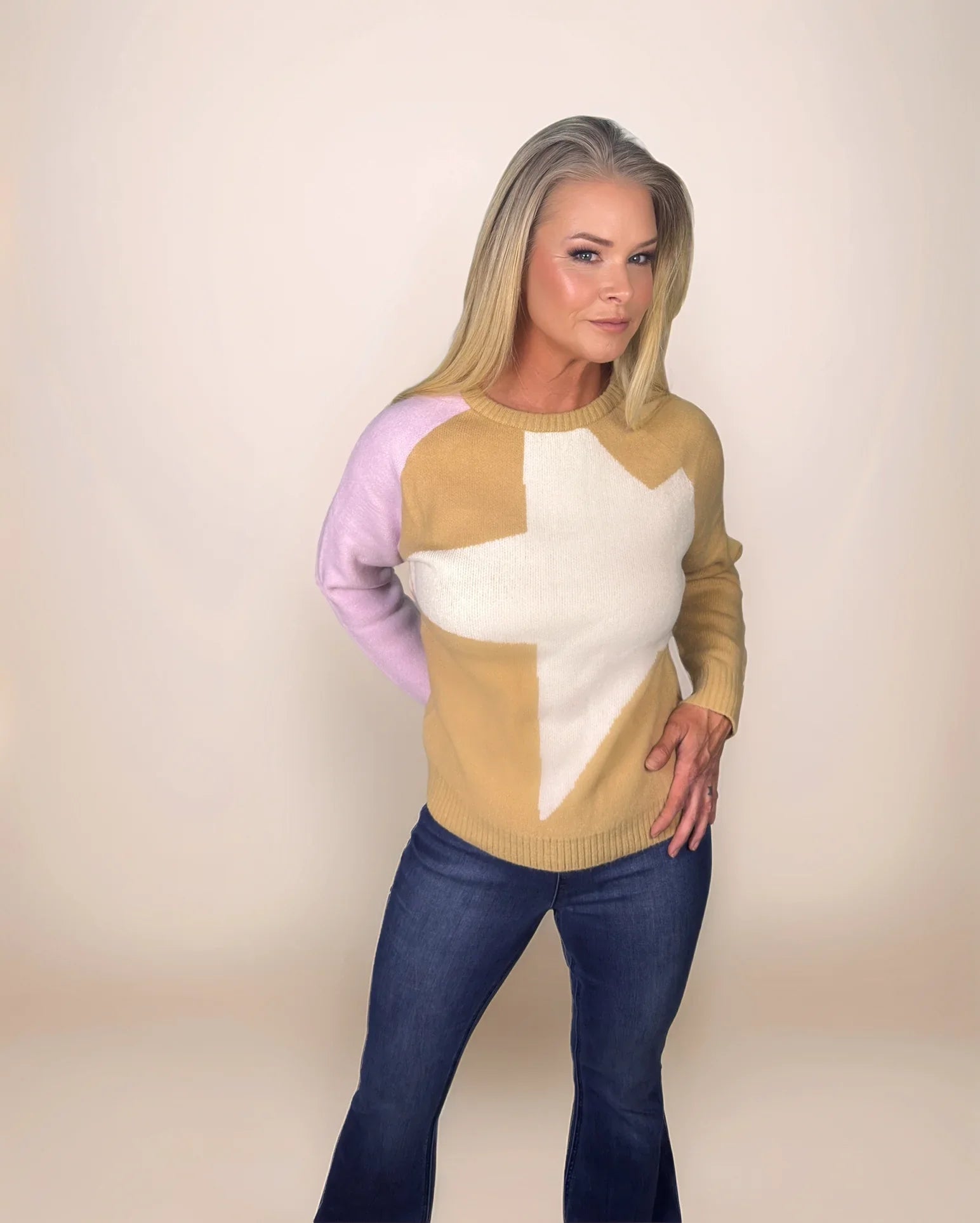 a fashion forward blonde woman is wearing a colorblock sweater in camel and pink with a cream star on the front
